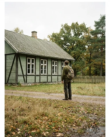A person standing outdoors near a small school building, seen from a distance, not facing the camera