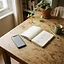 A phone lying face up on a wooden table beside an open notebook