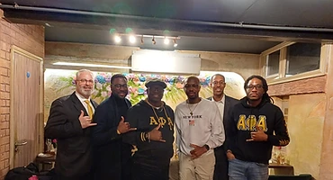Brothers gathered at a restaurant wearing Alpha Phi Alpha letters