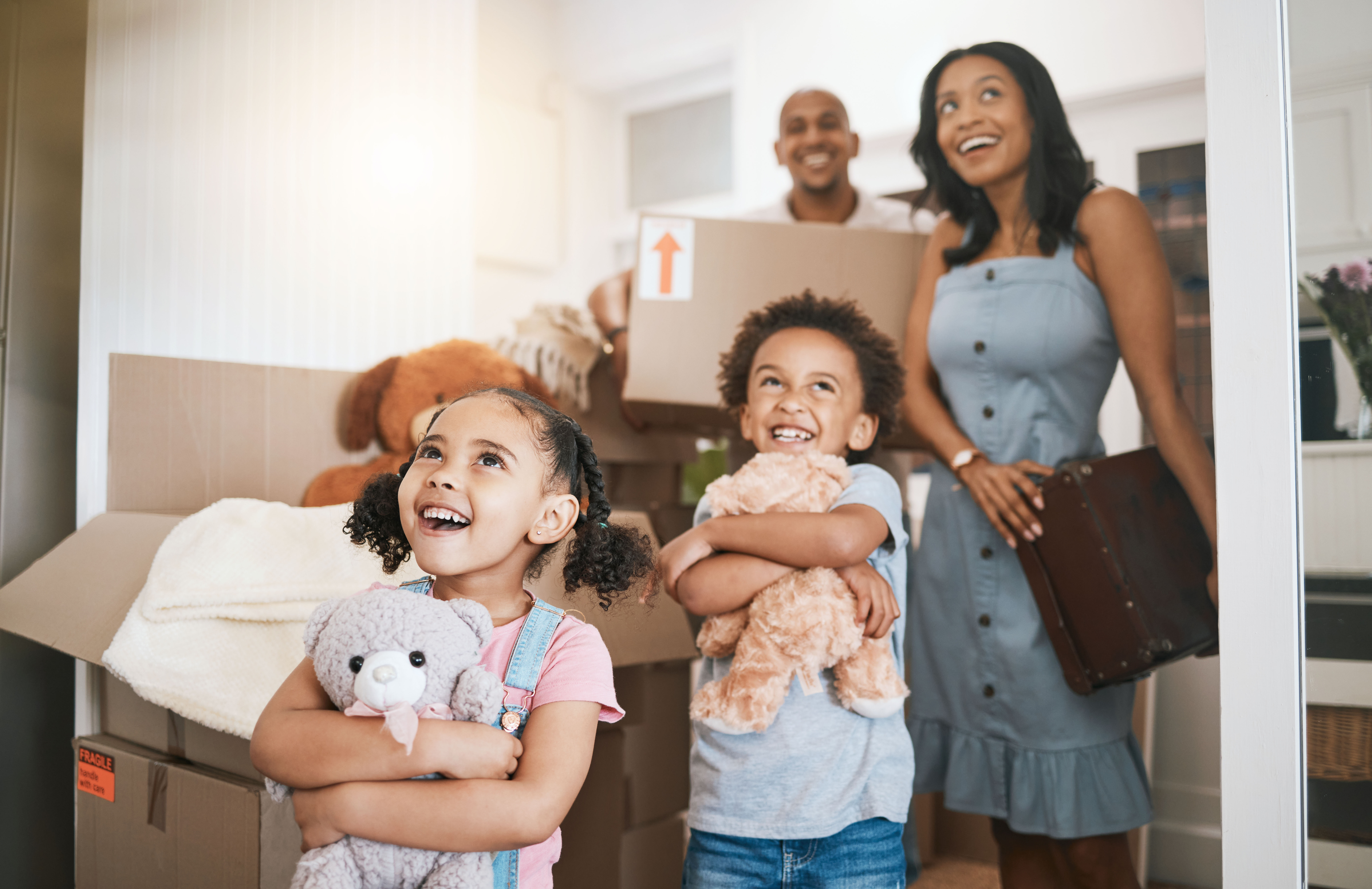 A family moving into their new home, children smiling with teddy bears among moving boxes
