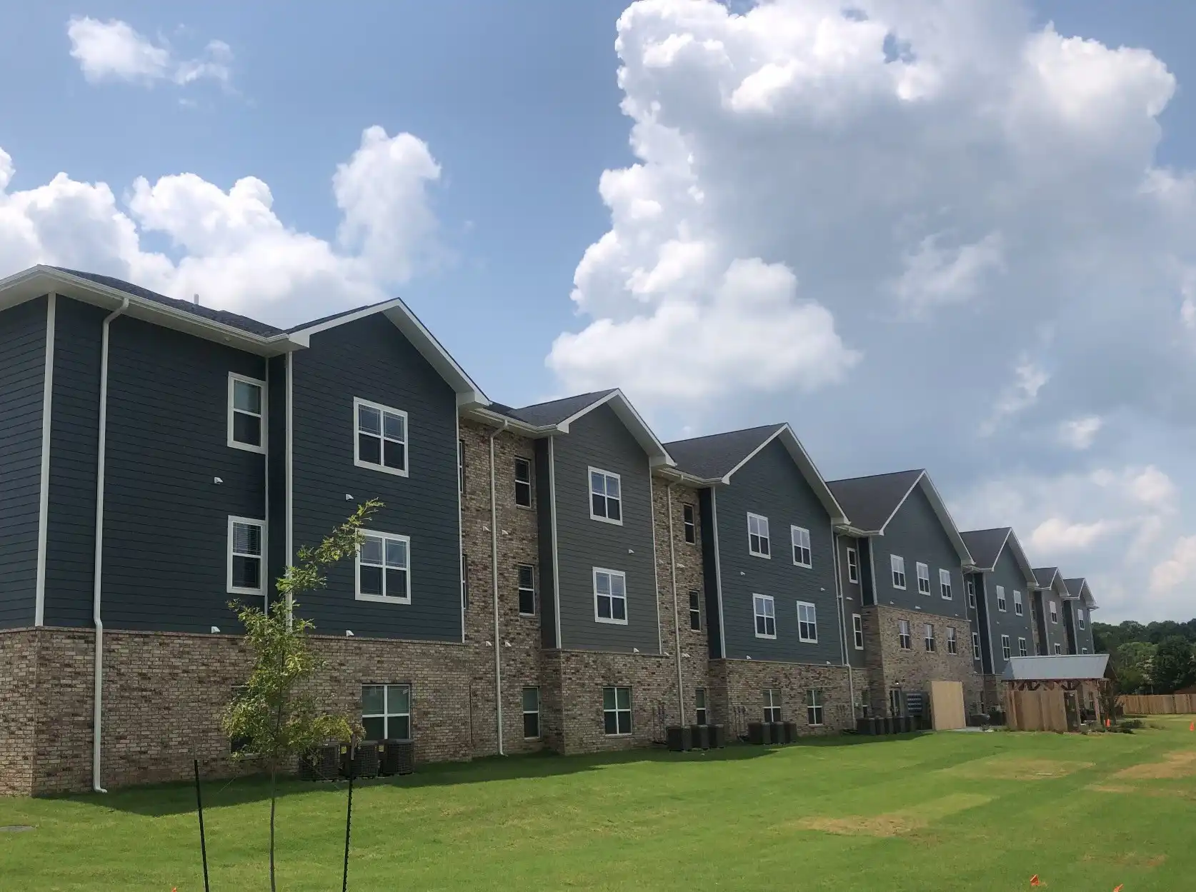 Trinity Housing Development multifamily community with blue-grey siding and brick exterior under a partly cloudy sky