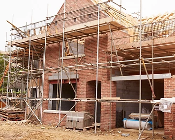 Brick residential home under construction with scaffolding and exposed roof framing