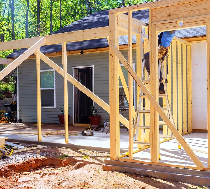 Wood framing for a home addition under construction alongside an existing house