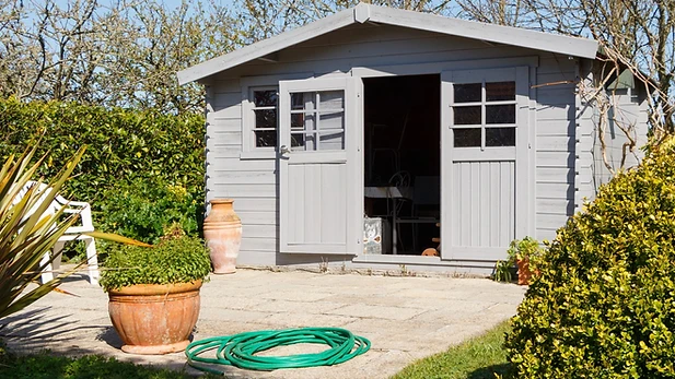 Small gray backyard building with open double doors and surrounding garden