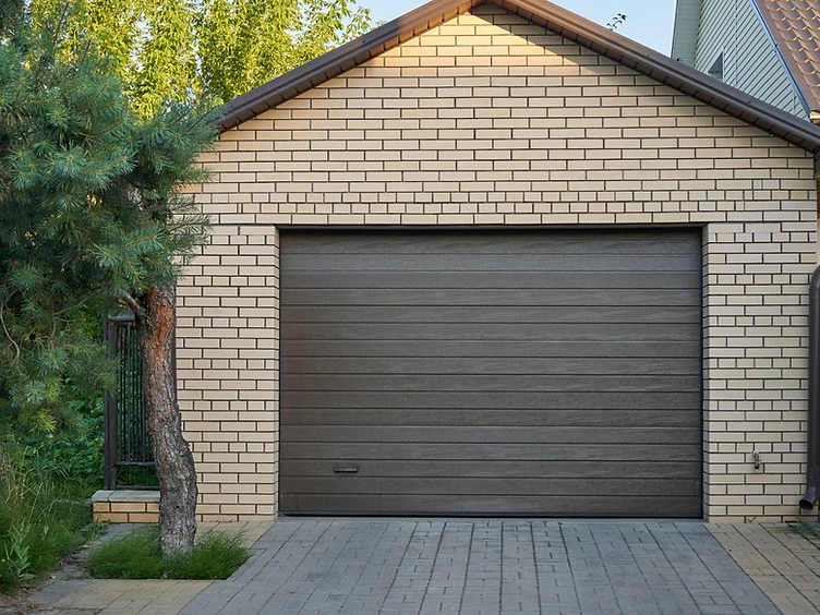 Brick residential garage with a dark sectional door and paved driveway