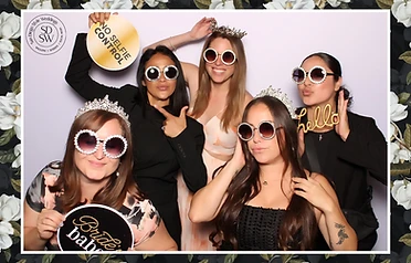 Five women in tiaras and rhinestone glasses with a gold sign