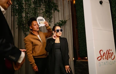 Couple posing with a strike a pose prop beside a Selfie Station kiosk