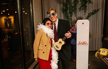 Woman in feather boa and man with ukulele at a Selfie Station
