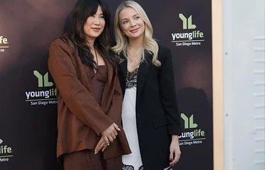 Two women on a branded step and repeat backdrop