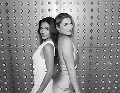 Two guests posing back-to-back at a glam event