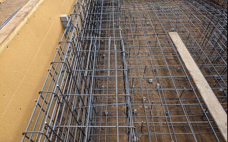 Close-up of a pool floor rebar grid with concrete spacer blocks holding the mat above the soil
