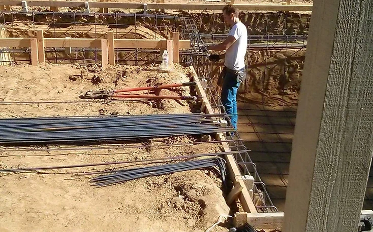 Worker installing reinforcing steel inside an excavated pool basin