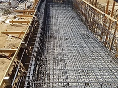 Long rectangular pool trench lined with a full rebar cage and wooden formwork beside a residence