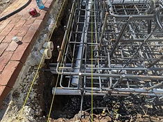 Close-up of a fountain rebar cage with Charlotte Pipe PVC conduits running through the lower steel and yellow layout strings across the brick patio