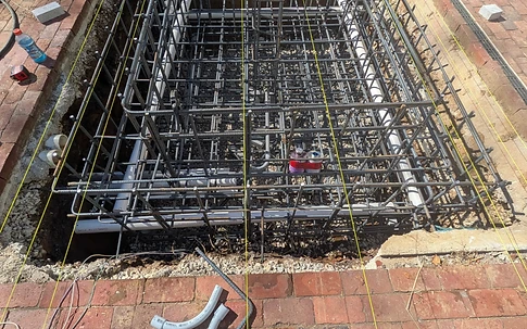 High-angle view of a box-in-a-box #5 rebar cage for a rectangular fountain foundation surrounded by brick pavers and string lines