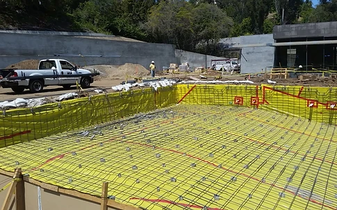 Rectangular pool excavation with yellow waterproofing membrane and rebar grid laid over it