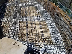 Multi-tiered excavation with rebar cages, vertical PVC plumbing riser, and wooden bracing