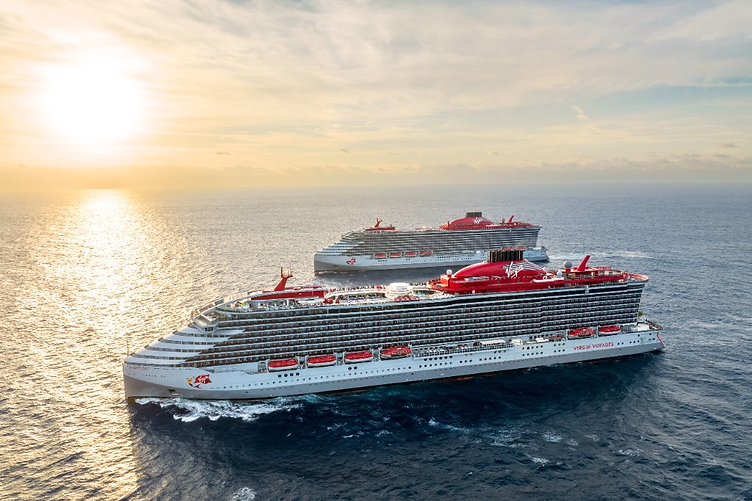Two Virgin Voyages cruise ships with red accents sailing on the ocean at sunset