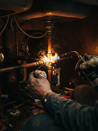Surge Plumbing soldering copper pipes under a kitchen sink