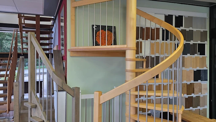 Wendeltreppe aus Holz vor einer Wand mit Holzmustern in der Ausstellung
