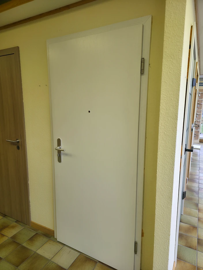 Innenansicht einer weißen Wohnungseingangstür mit Türspion und Griff
