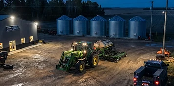Farm equipment dealership with tractor and seeding unit under yard lights in Stony Plain at dusk