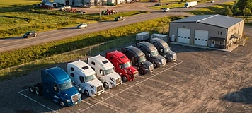 Day-cab tractors parked at a Woodstock transfer depot in the afternoon.