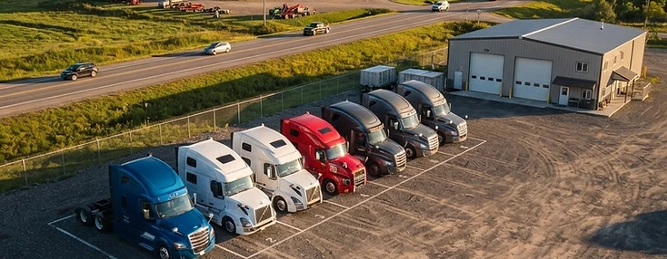 Day-cab tractors parked at a Woodstock transfer depot in the afternoon.