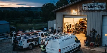 HVAC service van and utility truck at an open shop bay in Okotoks with the Sheep River valley behind at dusk