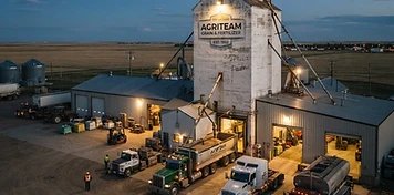 Grain elevator and farm-supply warehouse yard with delivery trucks at loading bays near Wainwright at dusk