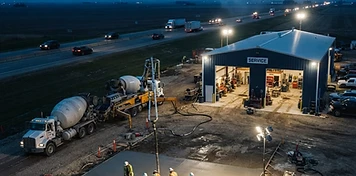 Concrete crew pouring a commercial slab with pump truck under night floodlights in Blackfalds at dusk