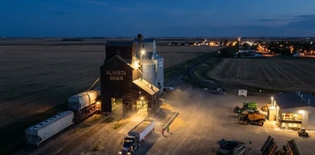 Grain elevators with a grain truck unloading and an ag dealership yard near Strathmore at dusk