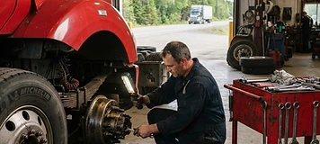 Mechanic inspecting the wheel assembly of a highway tractor inside a Saint-Léonard fleet maintenance shop.
