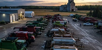 Agricultural equipment dealership yard with combines and air drills lined up for spring service at dawn in northeast Saskatchewan
