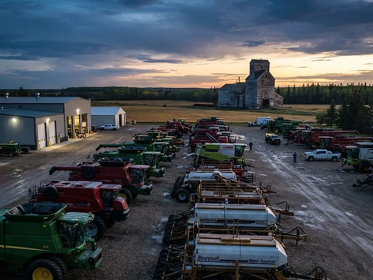 Agricultural equipment dealership yard with combines and air drills lined up for spring service at dawn in northeast Saskatchewan