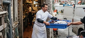 Chef receiving crates of fresh seafood at the back door of a Shediac coastal restaurant.