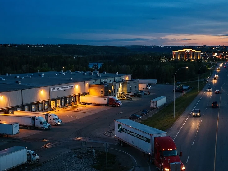 Distribution warehouses with a highway tractor pulling out onto the QEII corridor in Red Deer at dusk