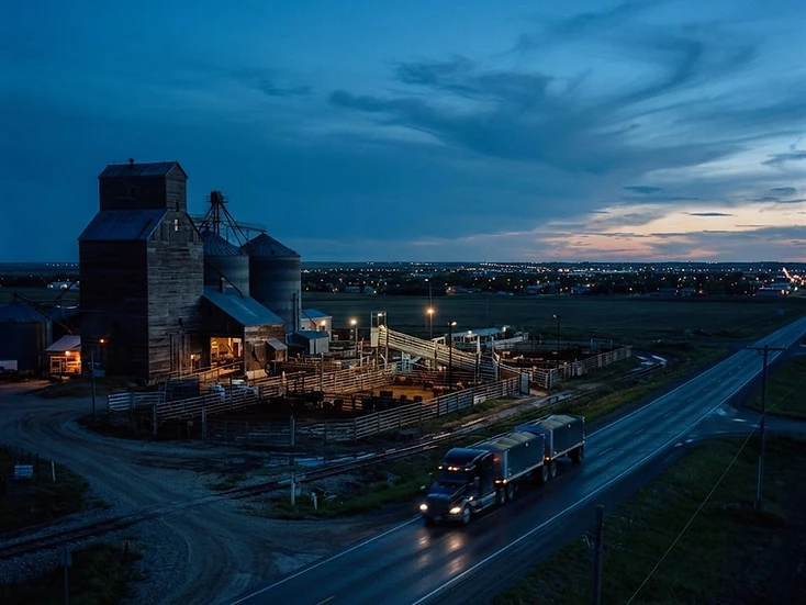 Grain elevators and cattle facilities at the edge of a southwestern Saskatchewan city at dusk