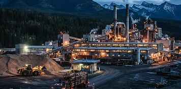 Pulp mill with recovery stacks and chip pile loader in Hinton with the mountain gateway horizon at dusk