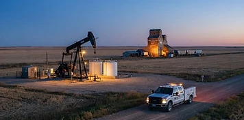 Pumpjacks beside a grain elevator on the west-central Saskatchewan prairie at dusk