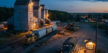 Grain elevators beside a rail line with a grain truck waiting at the scale in Camrose at dusk