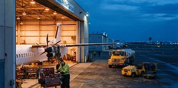 Aviation service hangar with a turboprop aircraft, mechanic and fuel truck on the apron in Leduc at dusk