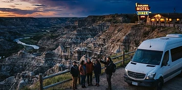 Tour shuttle van and visitors at a badlands viewpoint with hoodoo rock formations and a warmly lit motel and diner sign in Drumheller at dusk