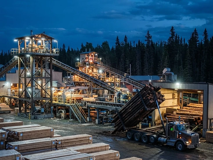 Sawmill with lumber sorting towers, conveyors and finished lumber stacks in Whitecourt at dusk