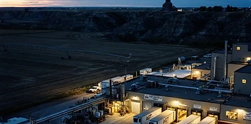 Food processing plant with refrigerated trucks and irrigated fields over the coulees in Lethbridge at dusk