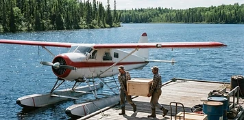 Crew loading supply crates onto a floatplane at a bright eastern Manitoba lake dock