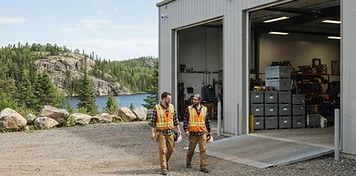 Contractors walking toward open service bays at a bright northern Manitoba industrial services yard