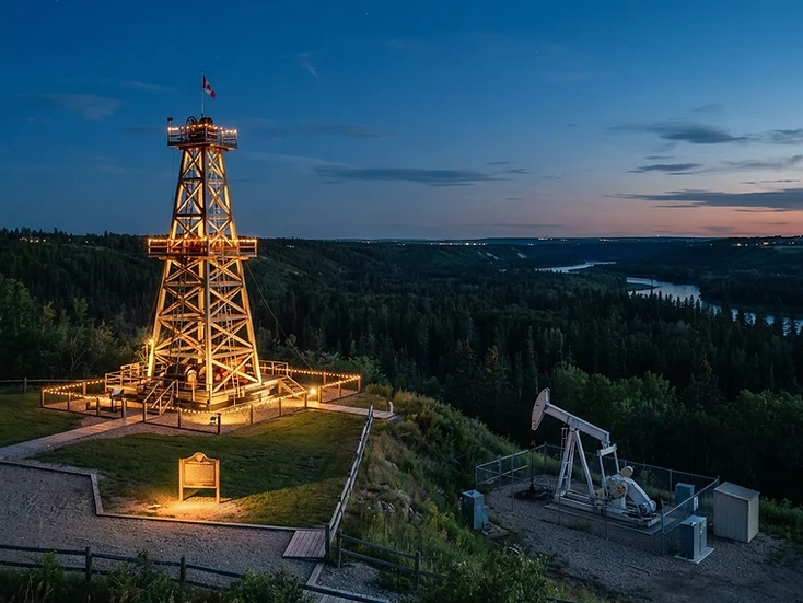 Heritage oil derrick monument and a working pumpjack on the North Saskatchewan river valley edge at Devon at dusk