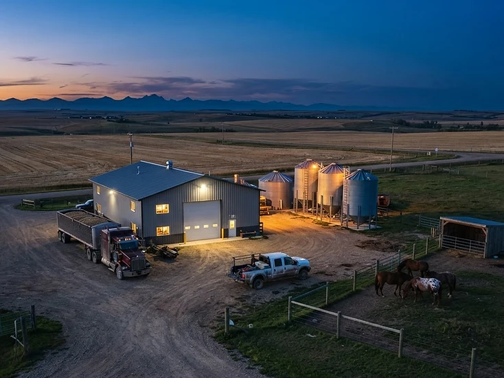 Farm shop and grain bins with a grain truck and farm pickup on Rocky View County prairie farmland at dusk