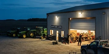 Farm equipment dealership lot with tractors and a swather under floodlights in Innisfail at dusk